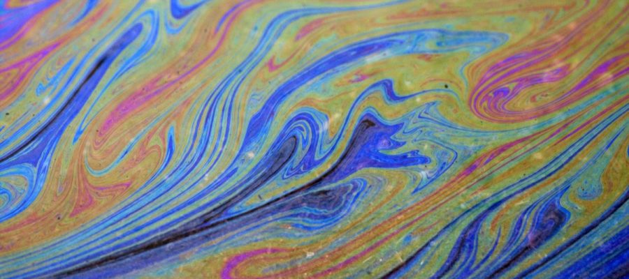 Photo carrée de détails d’une peinture abstraite formée de différentes courbes et lignes de peintures jaune, rose et bleu s’entremêlant sans se mélanger.